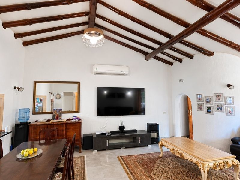Spacious open-plan living and dining area featuring a vaulted ceiling with exposed timber beams, tiled flooring, and a split-system air conditioner.