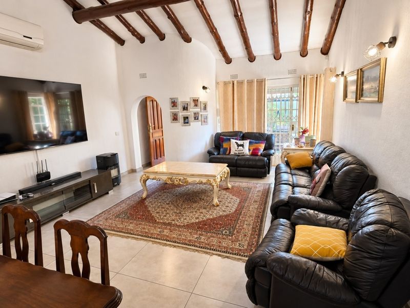 Spacious living room featuring exposed timber ceiling beams, tiled flooring, and an arched doorway leading to an outdoor area.