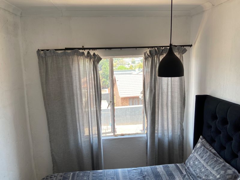 A bedroom featuring a casement window with a curtain rod and a modern pendant light fixture.