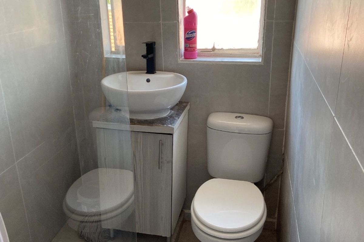 Compact bathroom featuring a modern vessel sink with vanity, toilet, and a glass-enclosed shower area with neutral wall and floor tiling.