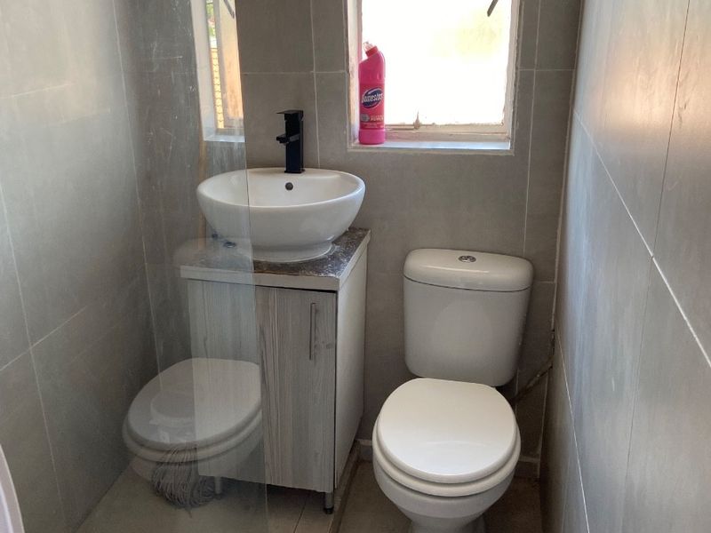 Compact bathroom featuring a modern vessel sink with vanity, toilet, and a glass-enclosed shower area with neutral wall and floor tiling.