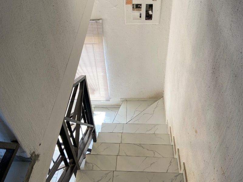 A staircase featuring marble-look tiled steps and a metal balustrade, requiring finishing touches to the surrounding walls and electrical board.