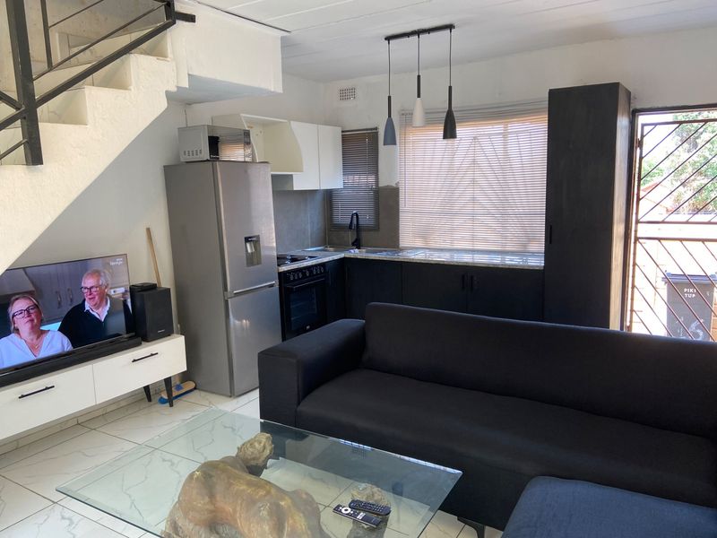 Open-plan living area featuring a compact kitchen with built-in cabinetry, oven, and hob, adjacent to a staircase and tiled living space.