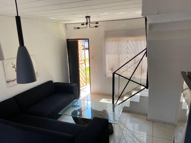 A bright living room featuring tiled floors, a staircase with a modern metal railing, and direct access to the exterior through a security gate.