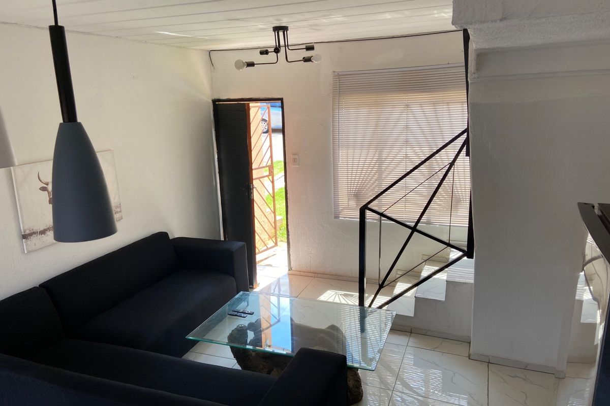 A bright living room featuring tiled floors, a staircase with a modern metal railing, and direct access to the exterior through a security gate.