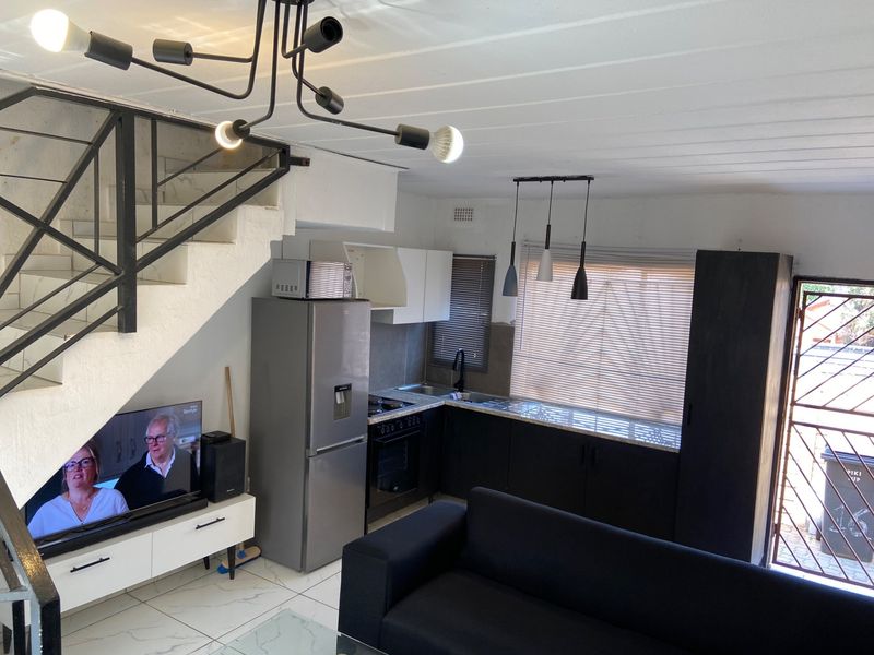 Open-plan living area featuring a compact kitchen with dark cabinetry, tiled flooring, and an integrated staircase leading to the upper level.