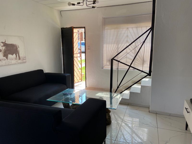 A living room featuring tiled floors, a staircase with a modern metal railing, and direct access to the exterior through a security gate.