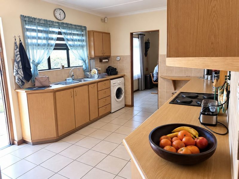 Functional kitchen featuring wooden cabinetry, laminate countertops, tiled backsplash, and integrated laundry plumbing, offering a practical layout with direct access to adjacent living areas.