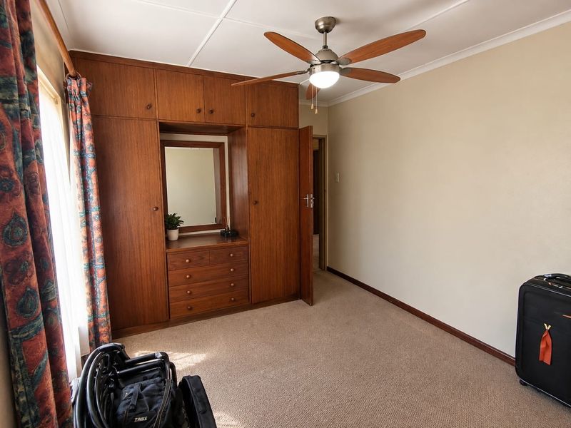 A bedroom featuring extensive built-in wooden cabinetry with an integrated vanity mirror, ceiling fan, and neutral carpeting.