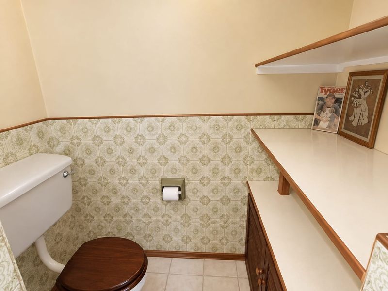 A functional bathroom featuring vintage patterned wall tiles, a toilet, and built-in wooden shelving for storage.