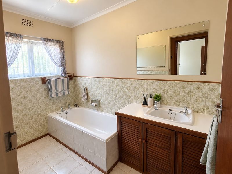 A functional bathroom featuring a built-in bathtub, a vanity cabinet with an integrated sink, and classic patterned wall tiling.