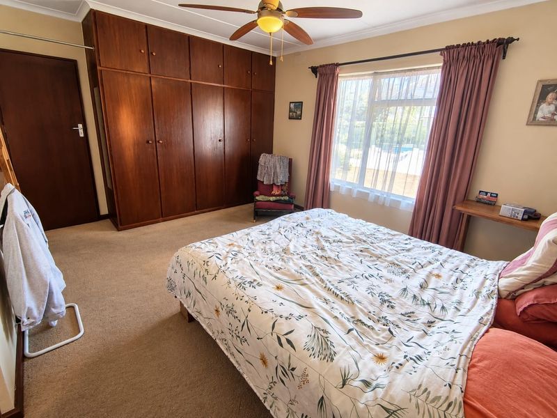 A bedroom featuring built-in wooden cupboards, a ceiling fan, and carpeted flooring, offering a functional space with natural light.