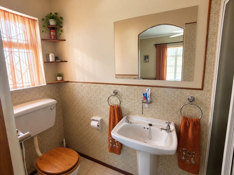 A functional bathroom featuring a pedestal basin, toilet, and wall-mounted mirror with classic tiled wall finishes and built-in corner shelving.