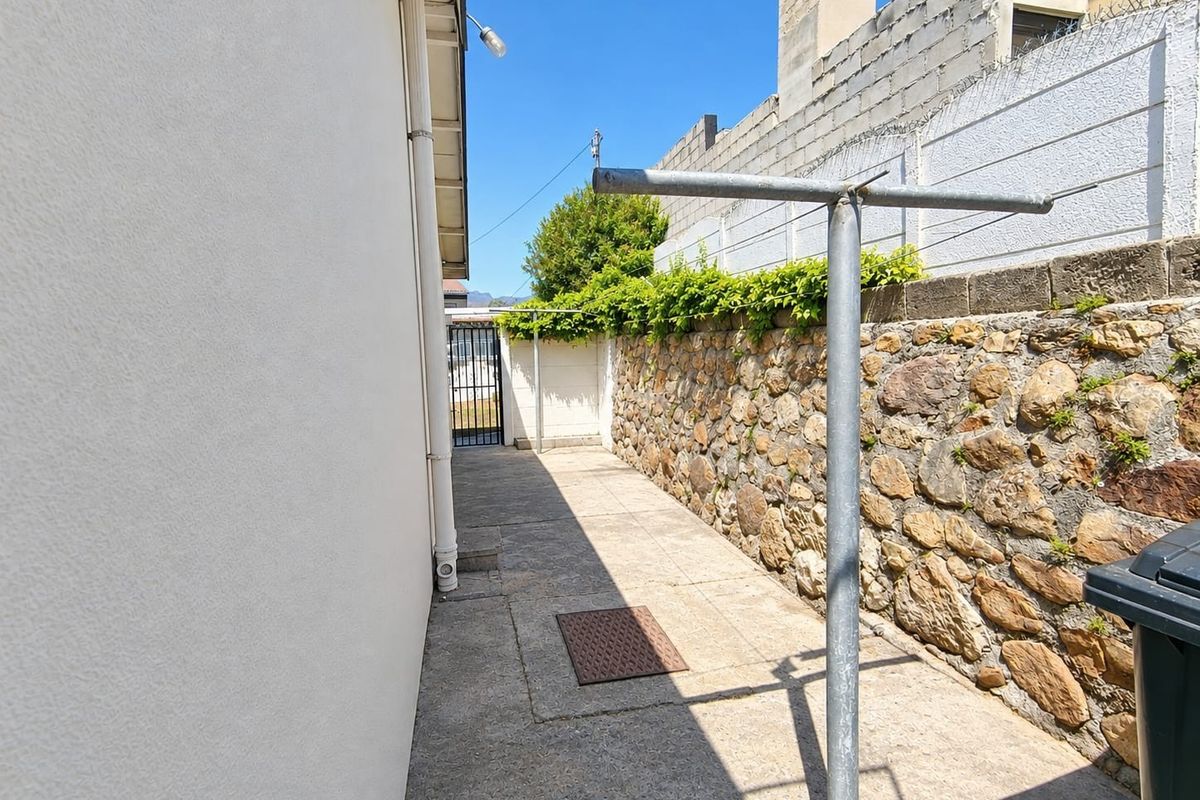 A side exterior area featuring a stone retaining wall, concrete paving, and a metal washing line, providing functional outdoor utility space.