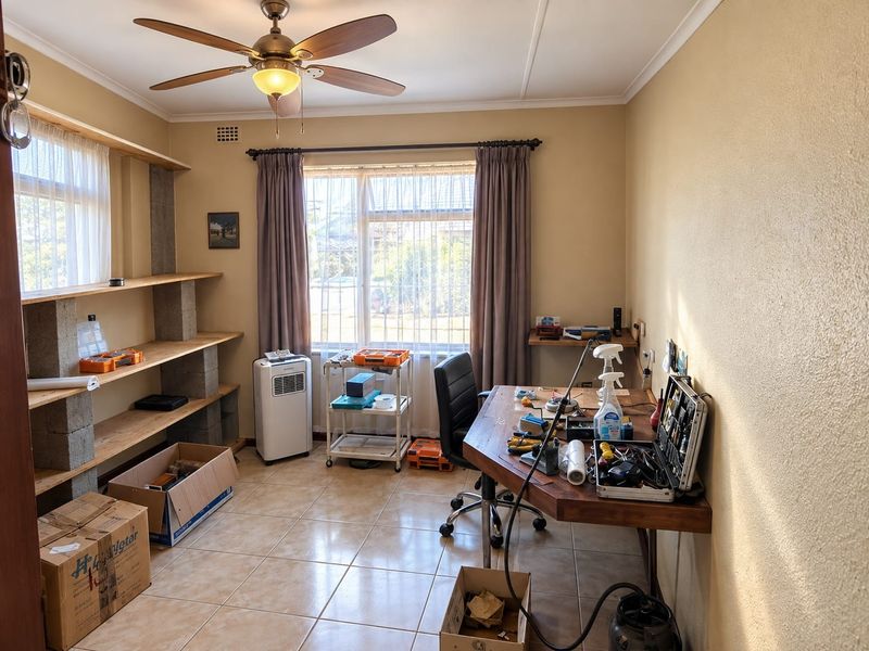 A functional home office space featuring tiled flooring, a ceiling fan, and built-in shelving units, providing a practical area for work or hobbies.