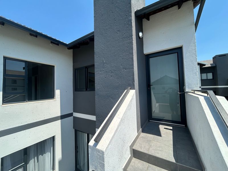 Modern townhouse entrance featuring a tiled staircase with metal handrail, glass panel door, and contemporary two-tone exterior facade.
