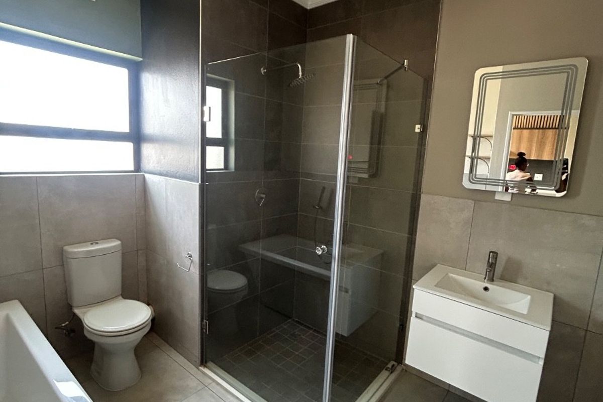 Modern bathroom featuring a glass shower enclosure, wall-mounted vanity with basin, bathtub, and neutral tiled finishes throughout.