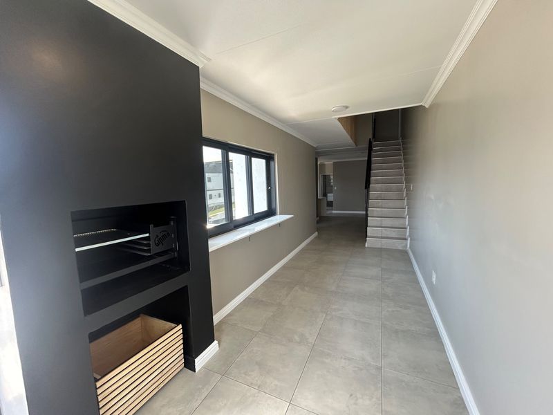 An open-plan living area featuring a modern built-in fireplace, tiled flooring, crown molding, and a staircase leading to the upper level.