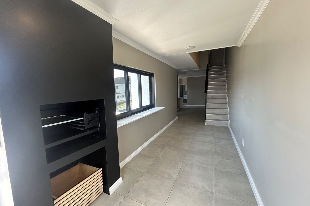 An open-plan living area featuring a modern built-in fireplace, tiled flooring, crown molding, and a staircase leading to the upper level.