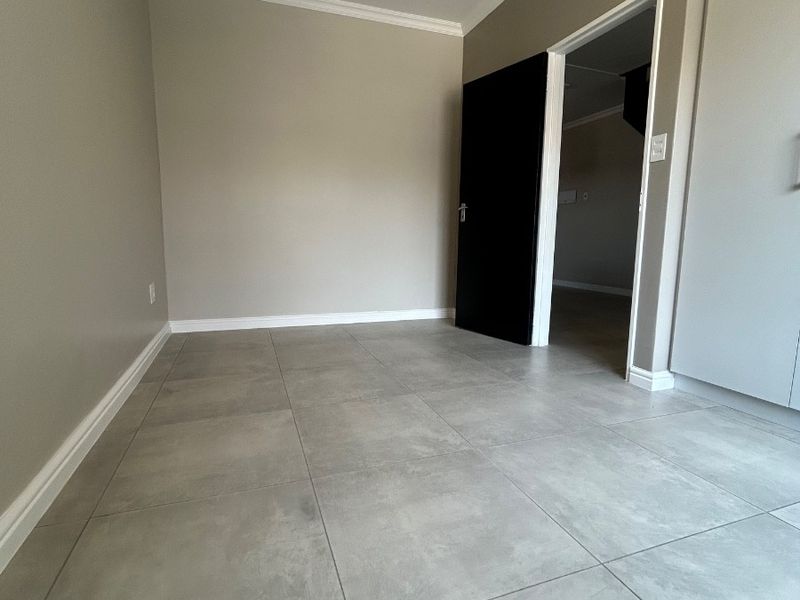A clean, empty bedroom featuring modern grey floor tiles, built-in cupboards, and neutral wall tones, ready for personalization.