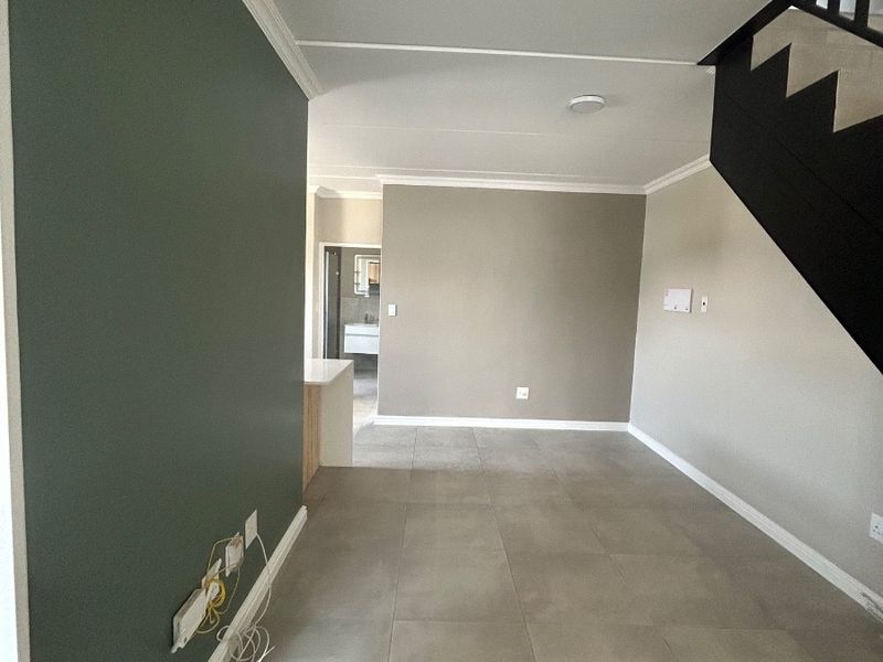 An open-plan living area featuring neutral tiled flooring, a modern staircase, and a feature wall, offering a clean and versatile space.