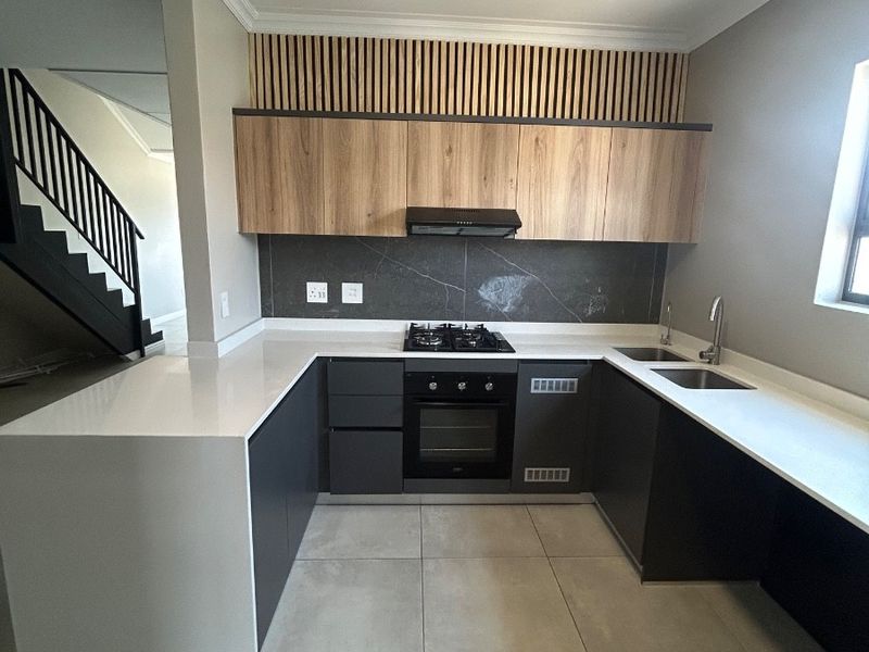 Modern U-shaped kitchen featuring sleek two-tone cabinetry, stone countertops, integrated gas hob, oven, and stylish slatted wood accent detailing.