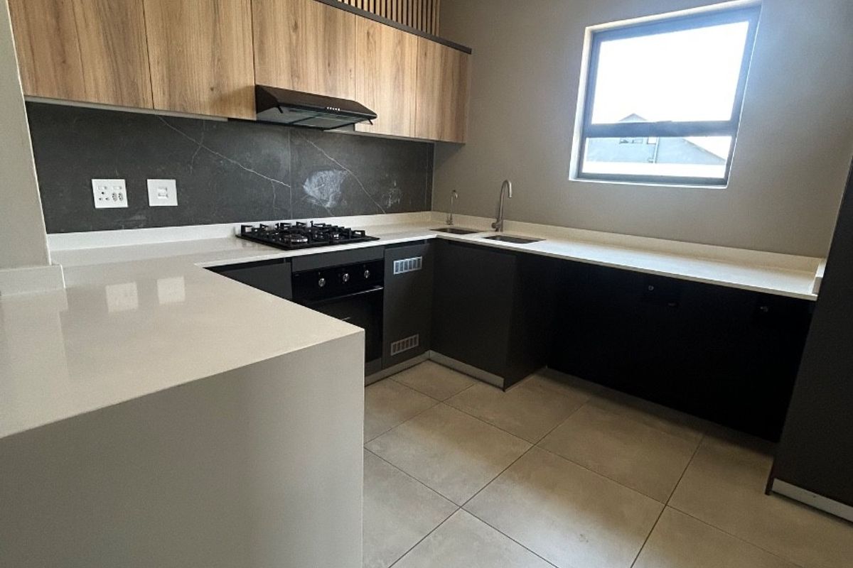Modern kitchen featuring sleek dark cabinetry, light wood accents, stone countertops, gas hob, built-in oven, and large format floor tiles.