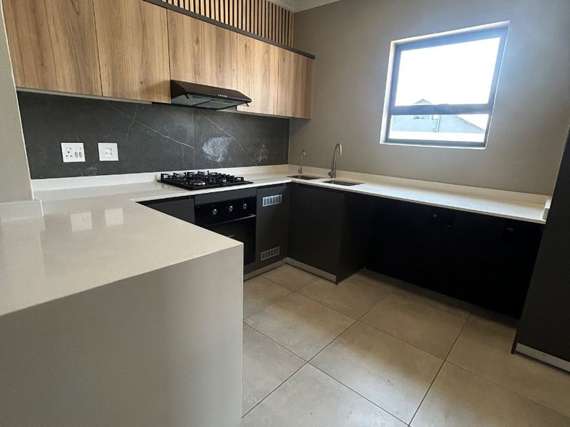 Modern kitchen featuring sleek dark cabinetry, light wood accents, stone countertops, gas hob, built-in oven, and large format floor tiles.
