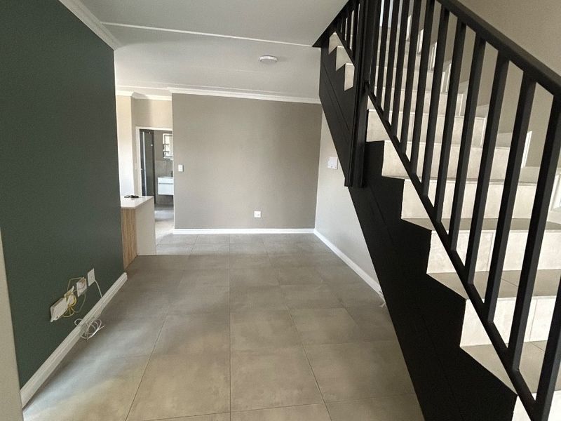 A bright, empty hallway featuring modern tiled flooring, a sleek black staircase with metal balustrades, and neutral wall finishes.