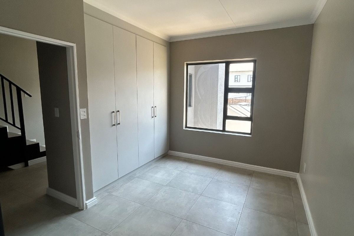 A bright, empty bedroom featuring neutral tiled flooring, built-in cupboards, and a modern aluminium window frame, offering a clean and versatile living space.