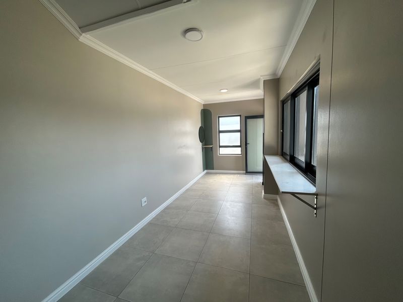 A clean, empty hallway featuring neutral-toned walls, tiled flooring, and modern aluminium window frames with a built-in wall shelf.