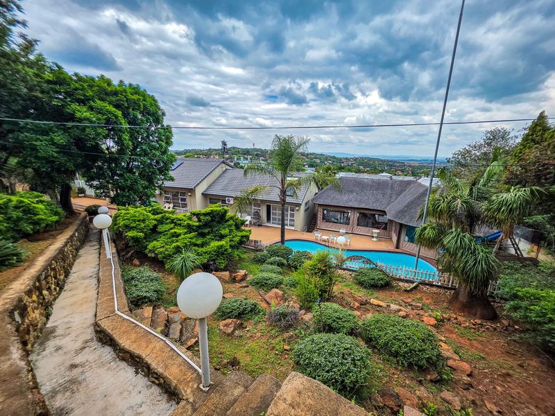 Elevated view of a residential property featuring a swimming pool, landscaped garden, stone retaining walls, and a mix of tiled and thatched roof structures.
