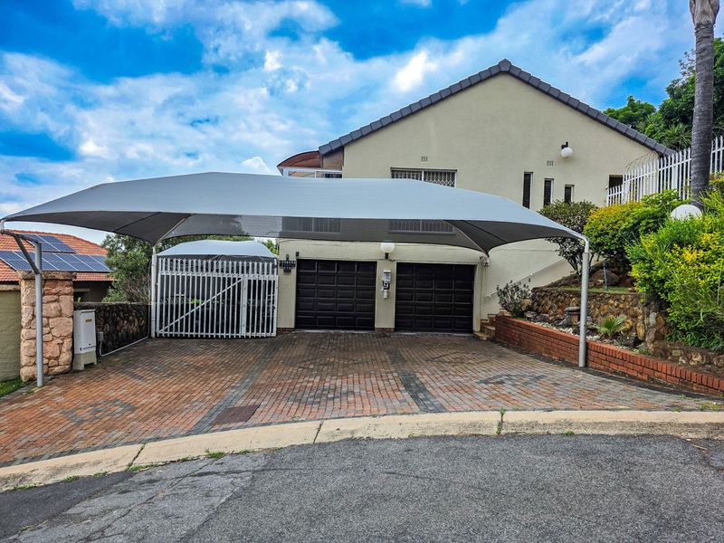 Front exterior view featuring a double garage, paved driveway, and a large shade sail carport, complemented by a stone retaining wall.