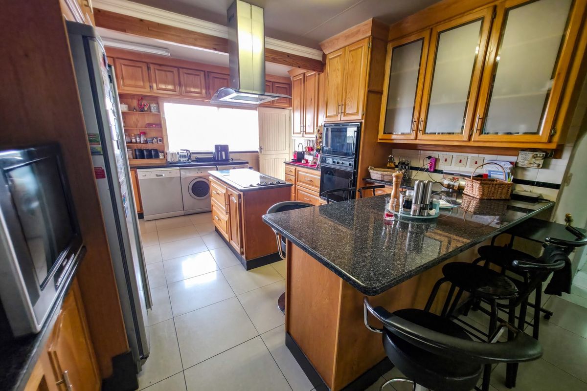 Spacious kitchen featuring wooden cabinetry, granite countertops, a central island with a cooktop, and integrated appliances, offering a functional layout for cooking and dining.