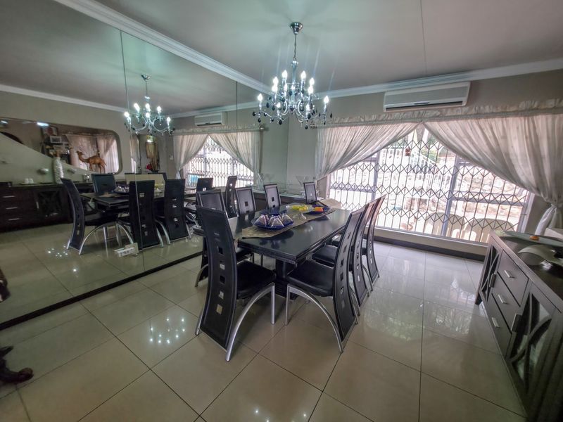 Spacious dining room featuring large mirrored wall, elegant chandelier, tiled flooring, and split-system air conditioning, providing a bright and functional space for entertaining.