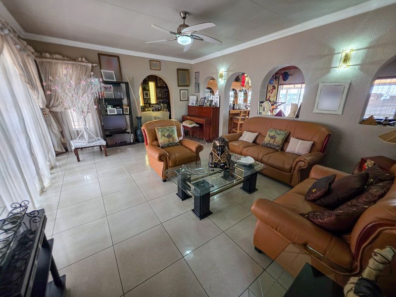 Spacious living room featuring tiled flooring, a ceiling fan, and distinctive arched wall openings leading to adjacent areas.