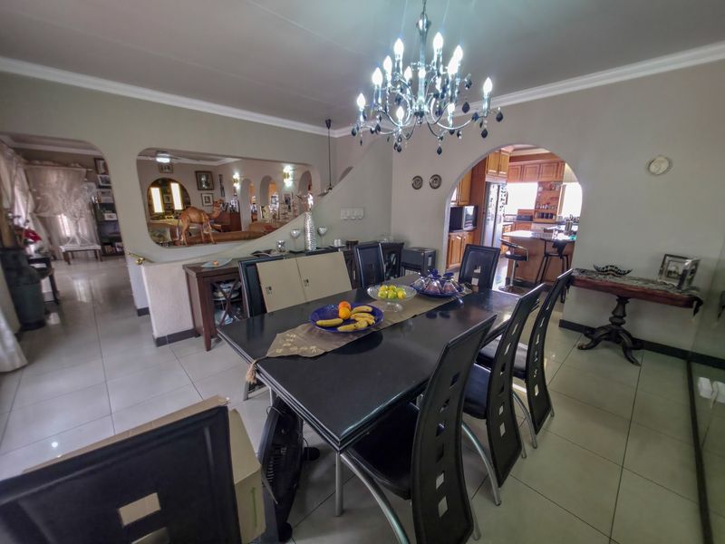 Spacious open-plan dining area featuring elegant chandelier lighting, tiled flooring, and an arched transition into the kitchen space.