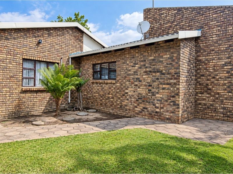 A well-maintained rear exterior view of a face brick house featuring a paved walkway, lawn area, and integrated satellite dish.