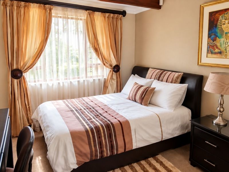 A cozy bedroom featuring neutral wall tones, carpeted flooring, and a window with curtains, providing a comfortable and functional sleeping space.