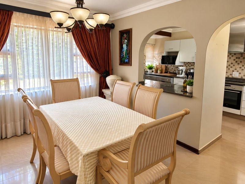Open-plan dining area featuring tiled floors and an arched transition into a modern kitchen with granite countertops and stainless steel appliances.