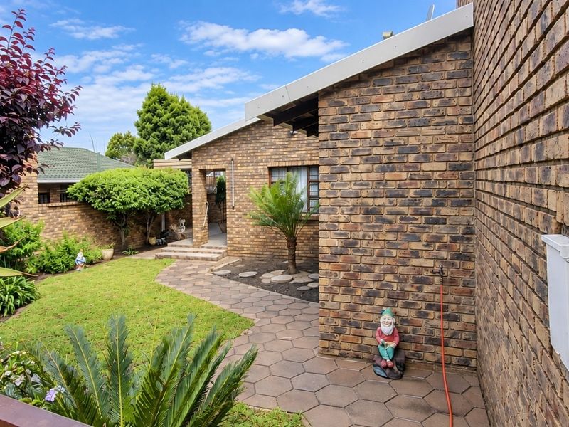 A well-maintained rear exterior view featuring a face brick facade, a paved walkway, and a landscaped garden area.