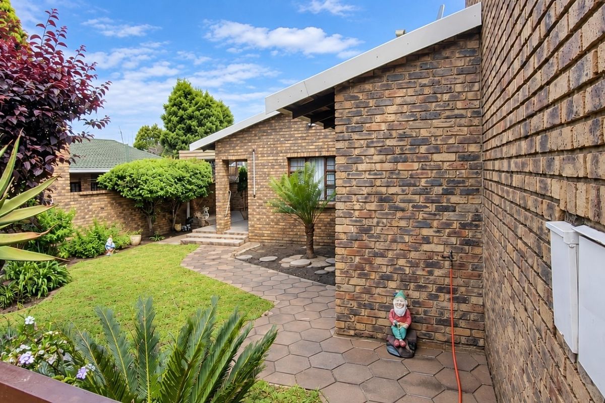 A well-maintained rear exterior view featuring a face brick facade, a paved walkway, and a landscaped garden area.