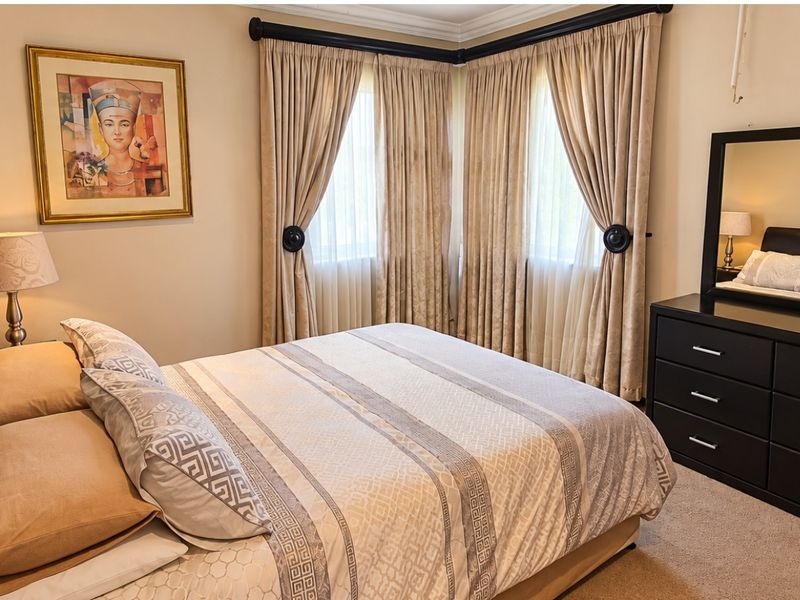 A well-maintained bedroom featuring neutral wall tones, carpeted flooring, and decorative cornice detailing.