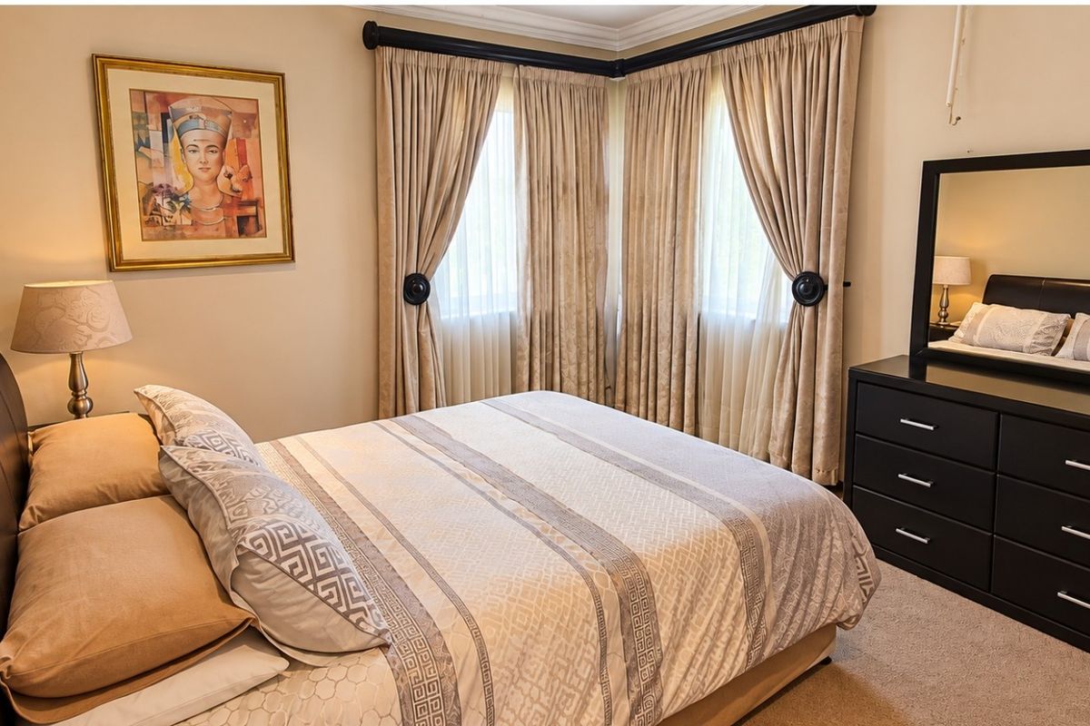 A well-maintained bedroom featuring neutral wall tones, carpeted flooring, and decorative cornice detailing.