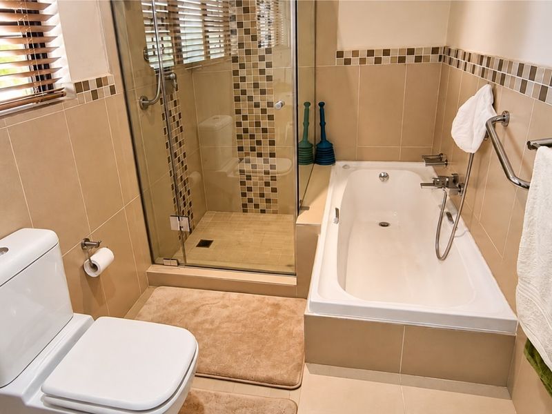 A well-maintained bathroom featuring a built-in bathtub, a separate glass-enclosed shower, and neutral wall tiling with a decorative mosaic border.