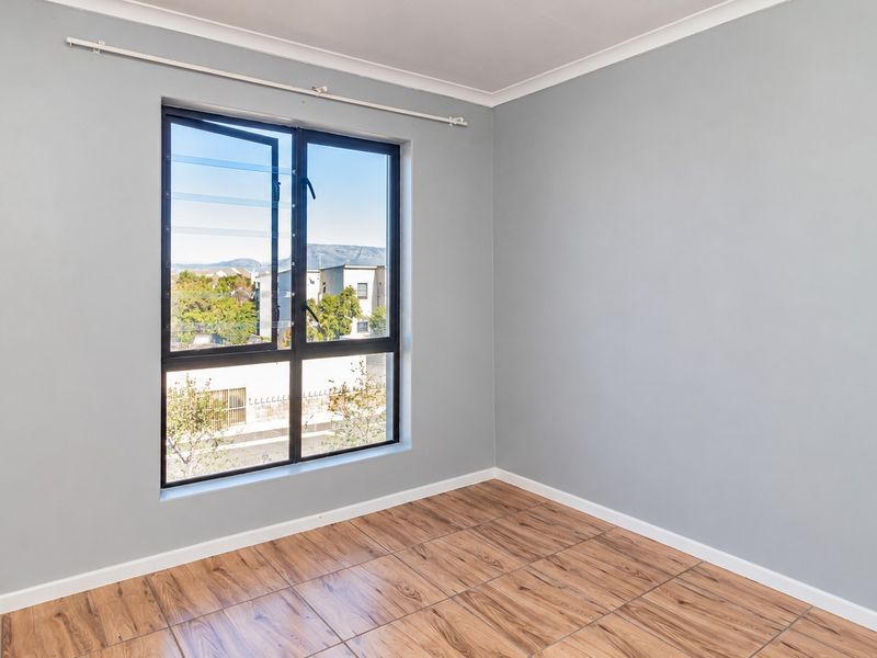 A bright, empty bedroom featuring modern wood-look tiled flooring, neutral grey walls, and a large aluminium-framed window with natural light.