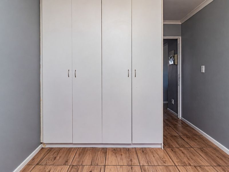 A clean, empty bedroom featuring neutral grey walls, wood-look tiled flooring, and white built-in cupboards.