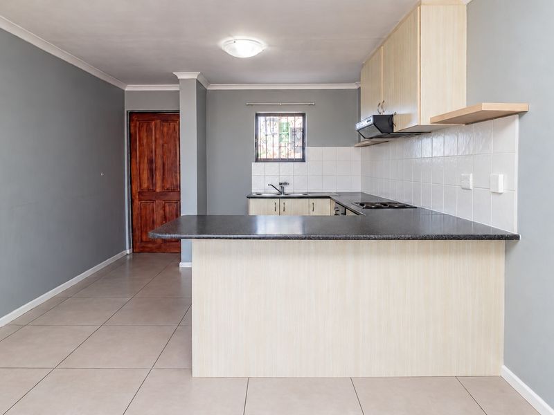 A functional kitchen featuring laminate cabinetry, a dark countertop, ceramic tile backsplash, and tiled flooring, presented in a clean, empty space.