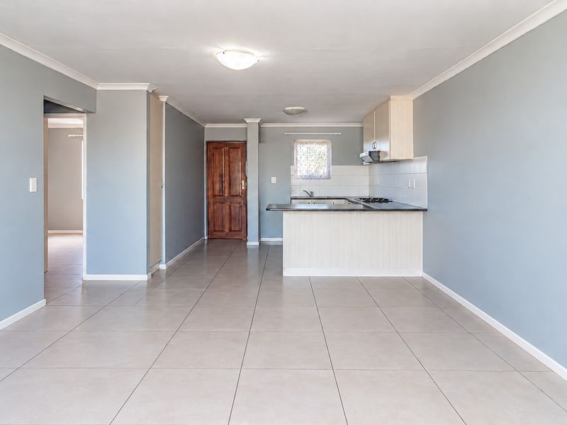 Spacious open-plan living area featuring neutral tiled flooring, soft grey walls, and a functional kitchen with built-in cabinetry and breakfast bar.