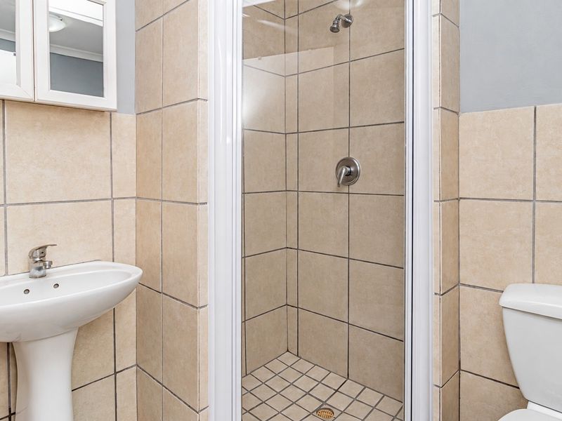 A functional bathroom featuring a pedestal basin, a tiled shower enclosure, and a standard toilet, finished with neutral wall tiling.